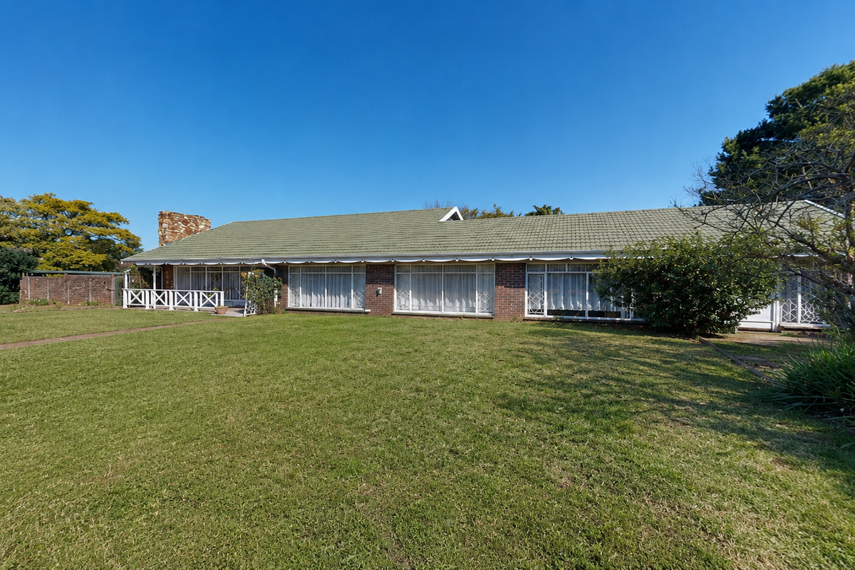 A spacious rear view of a single-story brick house featuring a tiled roof, a stone chimney, and a large, well-maintained lawn.