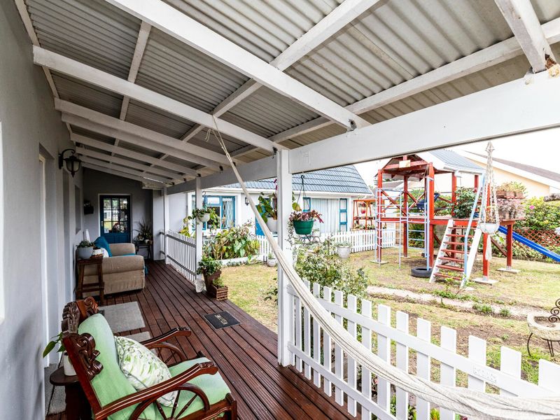 A covered timber deck patio overlooking a rear garden with a white picket fence and outdoor play area.