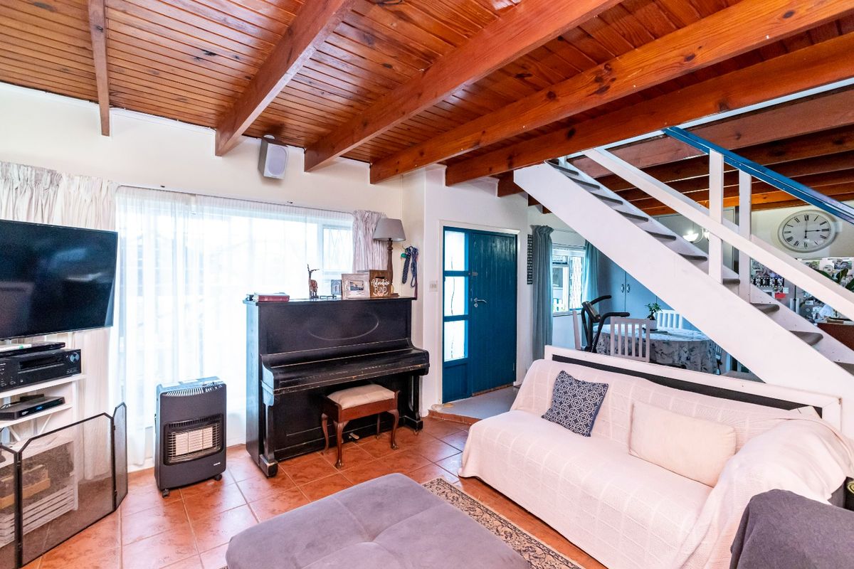 Open-plan living area featuring exposed timber ceiling beams, terracotta floor tiles, and a staircase leading to the upper level.