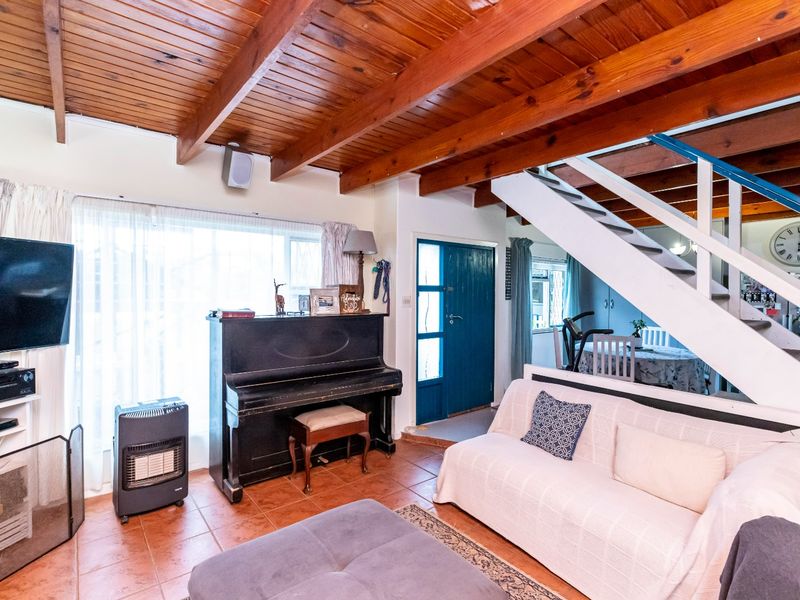 Open-plan living area featuring exposed timber ceiling beams, terracotta floor tiles, and a staircase leading to the upper level.