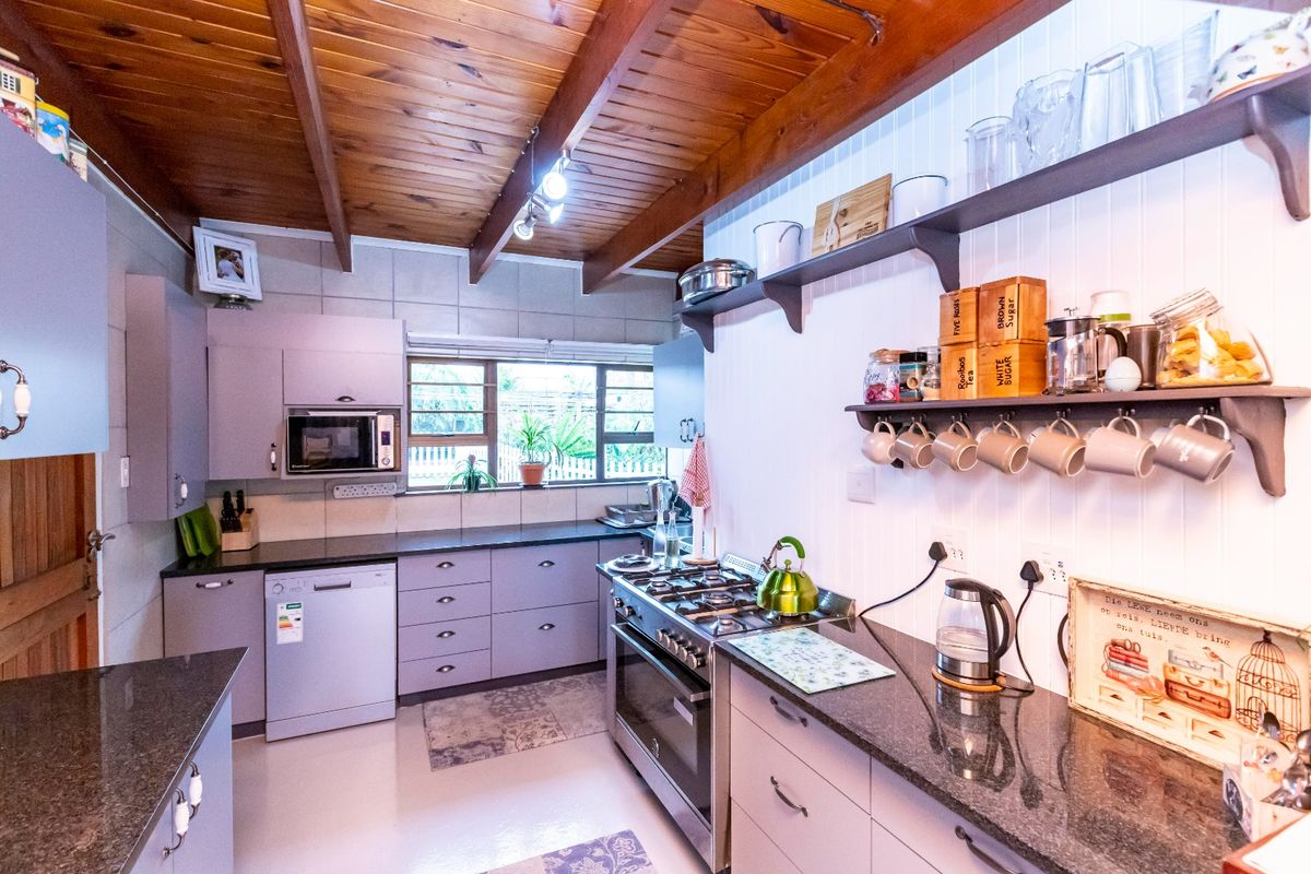 A well-appointed kitchen featuring granite countertops, a gas stove, built-in microwave, and a distinctive timber beam ceiling with open shelving.
