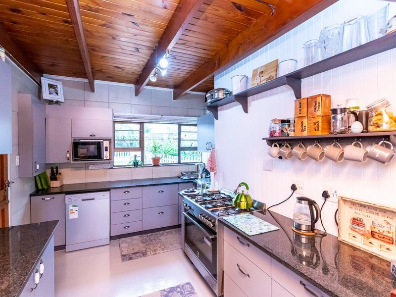 A well-appointed kitchen featuring granite countertops, a gas stove, built-in microwave, and a distinctive timber beam ceiling with open shelving.