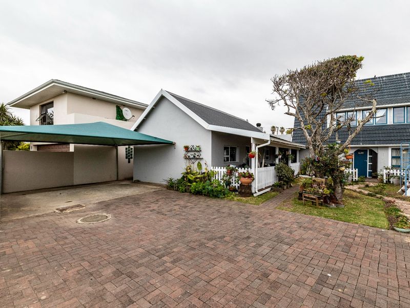 Front exterior view of the property featuring a paved driveway, a shade sail carport, and a small garden area with a picket fence.