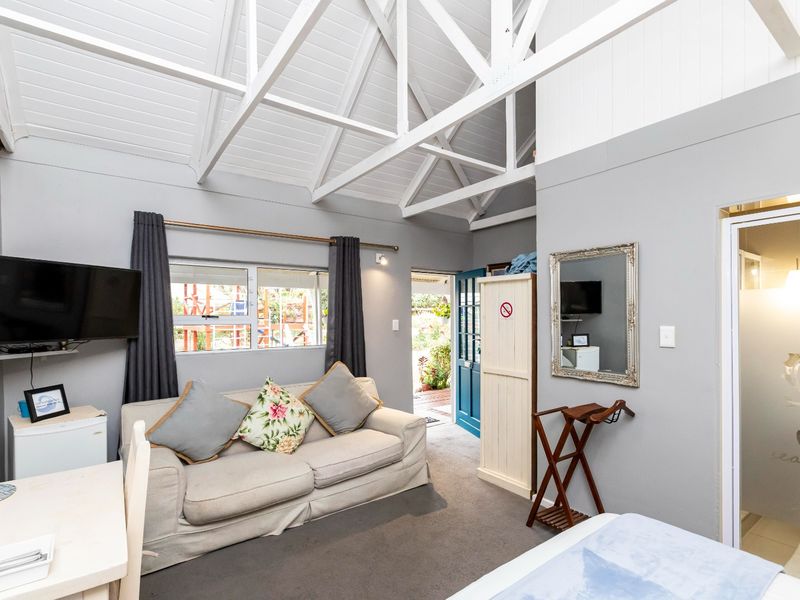 A cozy living area featuring a high vaulted ceiling with exposed white timber trusses, carpeted flooring, and direct access to an outdoor space.