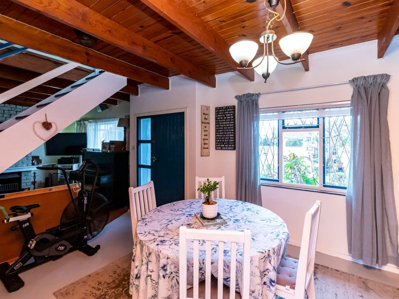 Open plan dining area featuring exposed timber ceiling beams, a staircase, and large windows with security bars, creating a functional and connected living space.