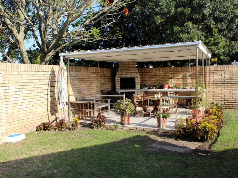 Outdoor covered patio area featuring a built-in brick braai, paved flooring, and enclosed by a brick boundary wall in a garden setting.