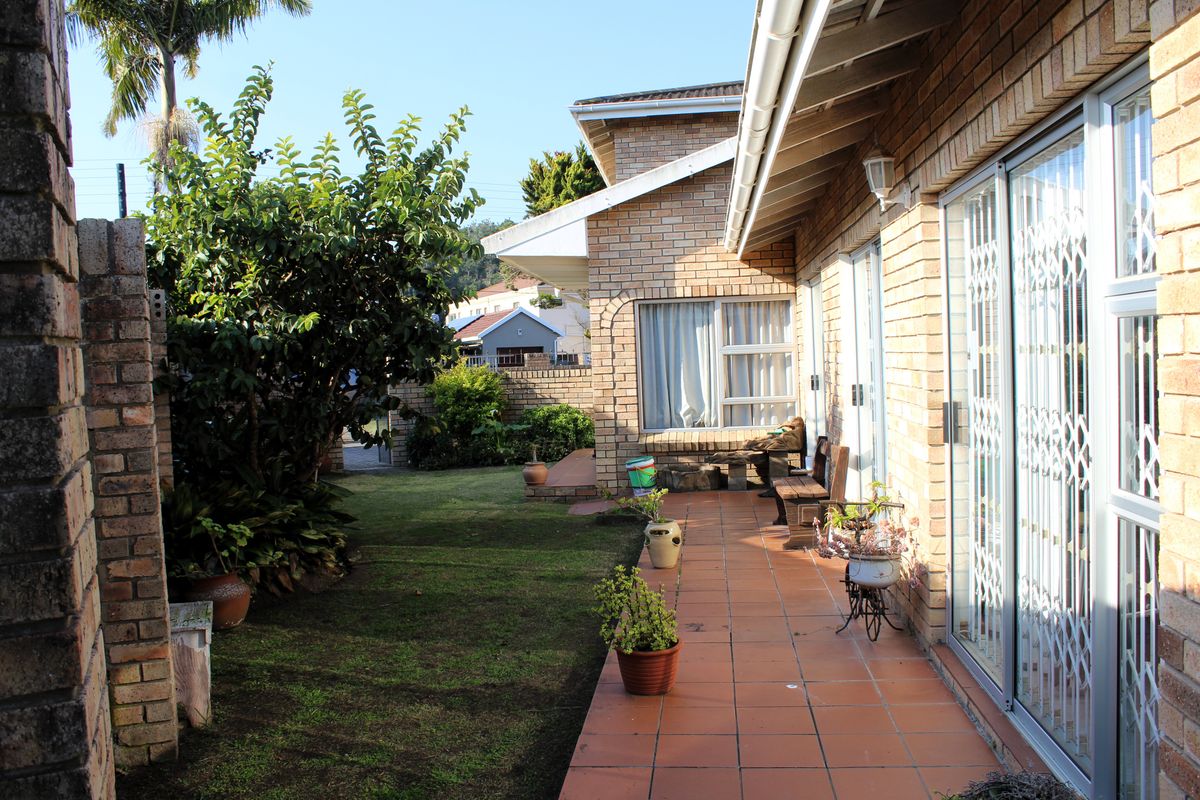 A rear exterior view of the house featuring a tiled patio, face brick facade, and sliding glass doors leading into the living area.