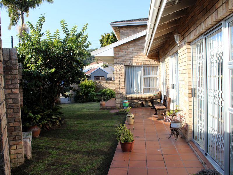 A rear exterior view of the house featuring a tiled patio, face brick facade, and sliding glass doors leading into the living area.
