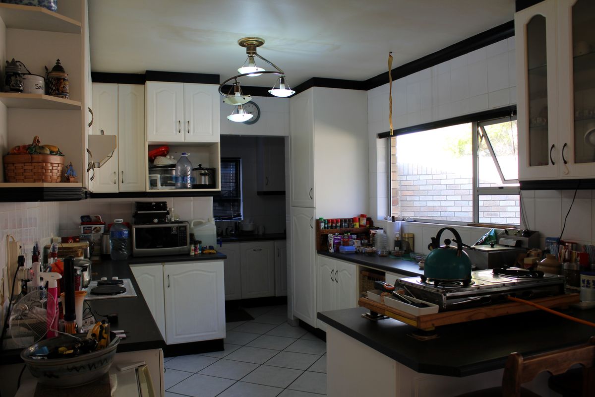 A functional kitchen featuring white cabinetry, dark countertops, tiled flooring, and a window, with visible water staining on the ceiling.