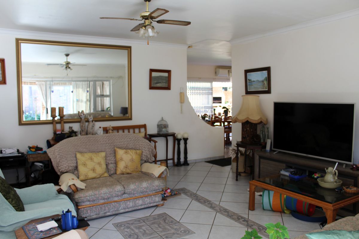 A living room featuring tiled flooring, a ceiling fan, and an arched opening leading to an adjacent dining area.