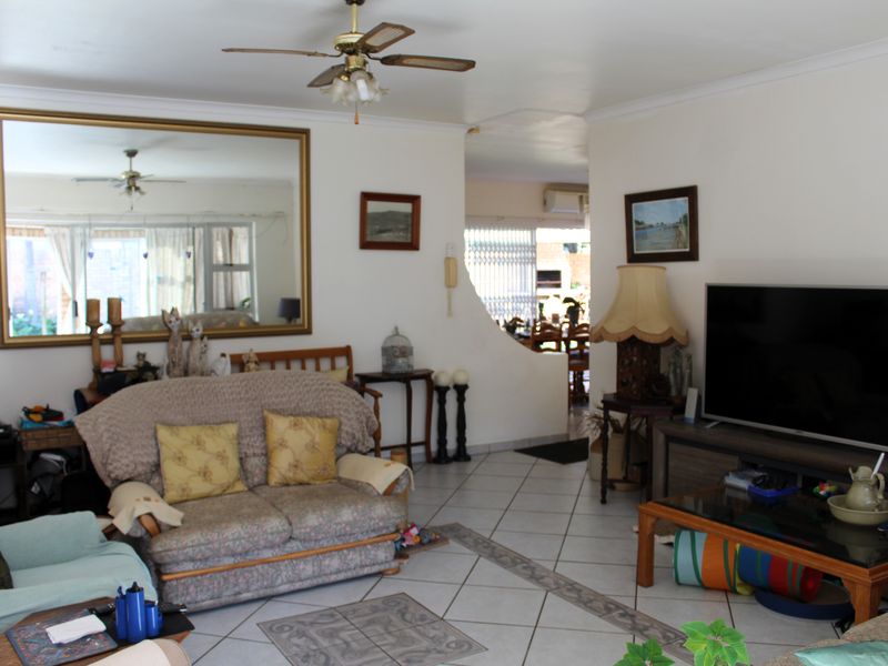A living room featuring tiled flooring, a ceiling fan, and an arched opening leading to an adjacent dining area.