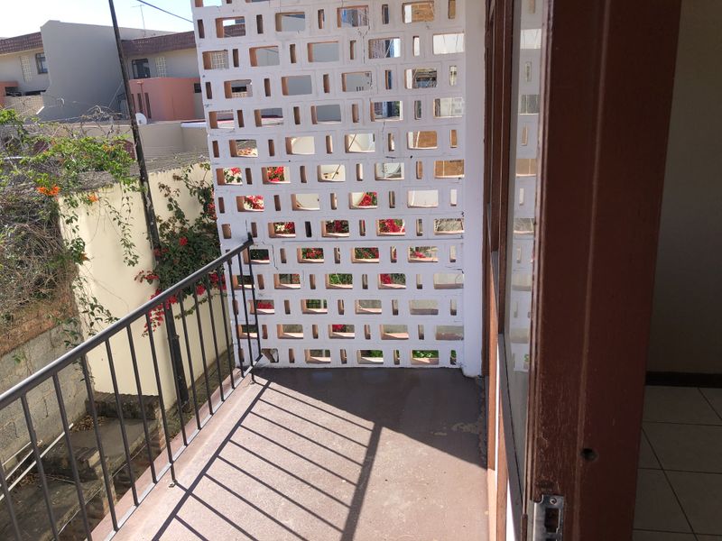 A balcony featuring a decorative breeze block privacy screen, metal railing, and tiled flooring, offering an outdoor space with a view of the surrounding area.