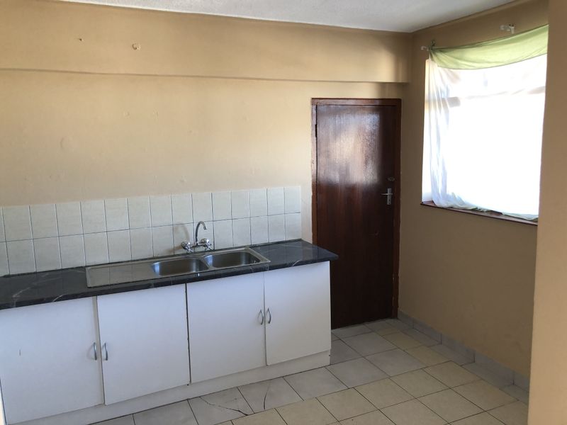 A functional kitchen area featuring a double bowl sink, laminate countertops, tiled splashback, and base cabinetry, requiring cosmetic updates to improve its condition.