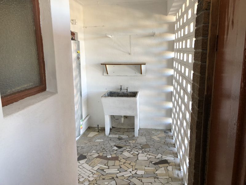 A functional laundry area featuring a traditional concrete utility sink, breeze block walling, and durable crazy paving flooring.