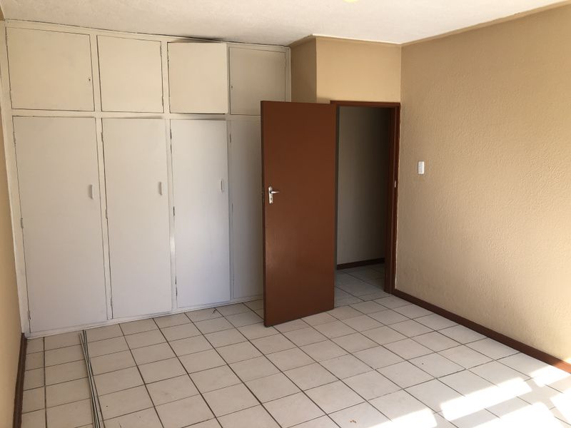 An empty bedroom featuring tiled flooring and built-in storage cupboards with a neutral wall finish.