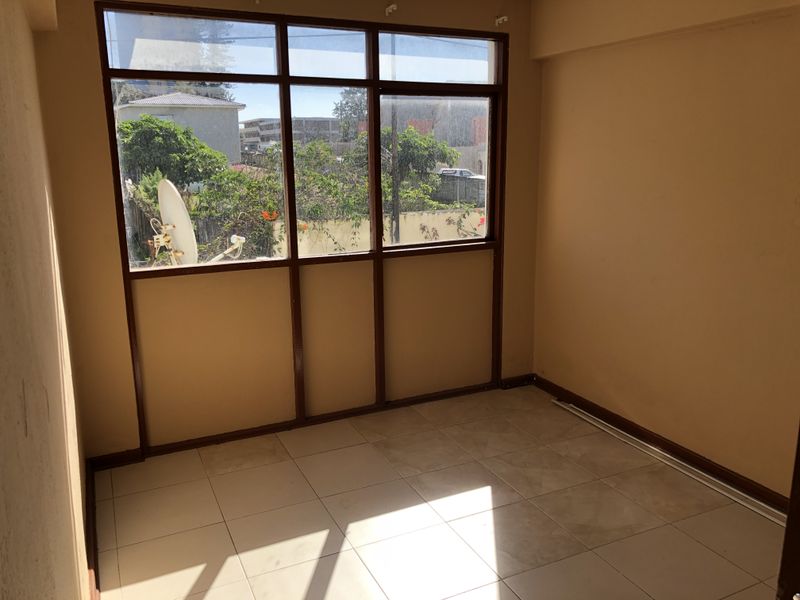An empty bedroom featuring tiled flooring and large windows with aluminium frames, offering natural light and a view of the surrounding area.