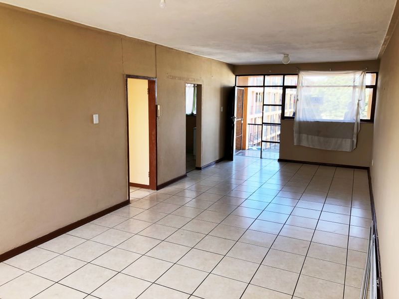 An empty, open-plan living area featuring tiled flooring, neutral wall tones, and direct access to a balcony through a sliding door.