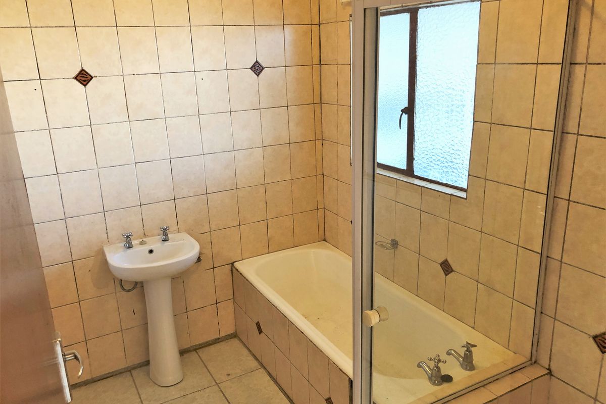 A dated bathroom featuring a pedestal basin, built-in bathtub with shower screen, and full-height wall tiling, offering potential for a modern renovation.