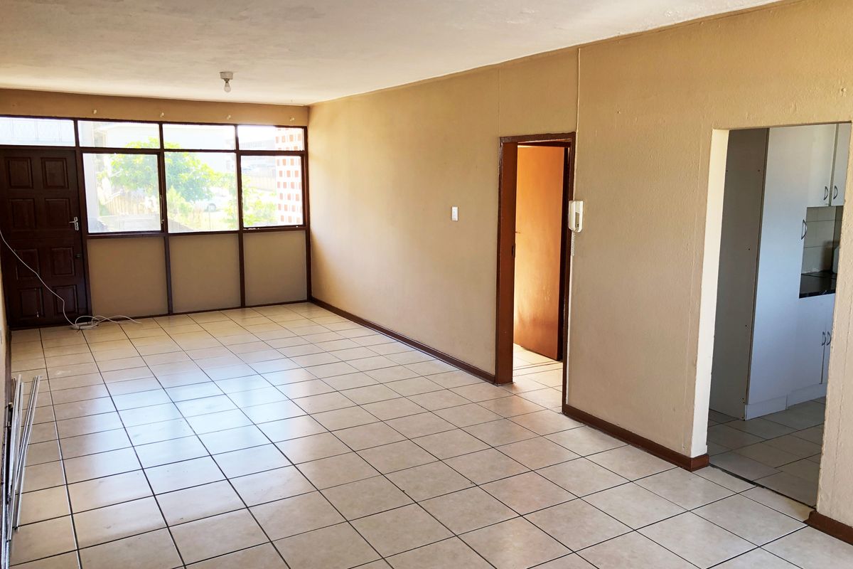 An empty, open-plan living area featuring neutral tiled flooring, large windows, and direct access to adjacent rooms.