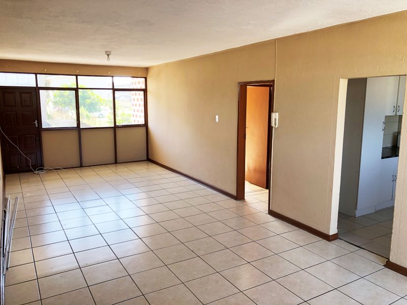 An empty, open-plan living area featuring neutral tiled flooring, large windows, and direct access to adjacent rooms.