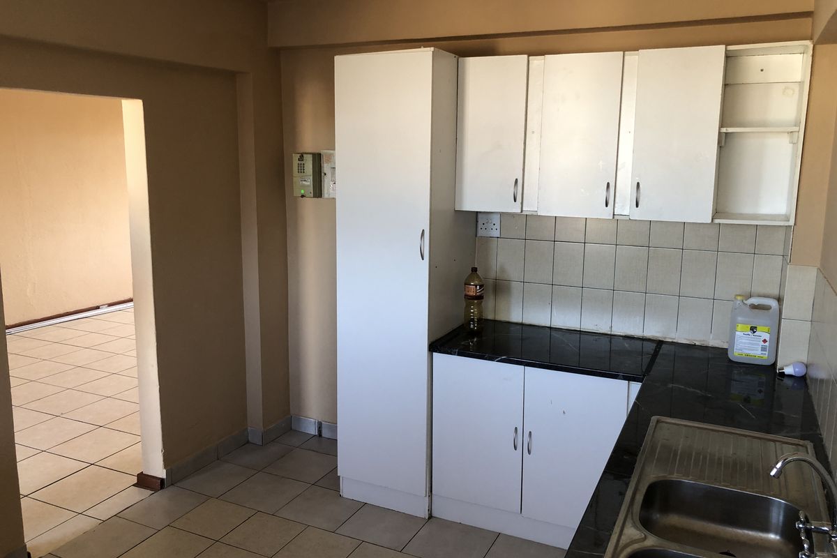 A functional kitchen featuring white built-in cabinetry, dark laminate countertops, a double stainless steel sink, and tiled flooring, ready for modernization.