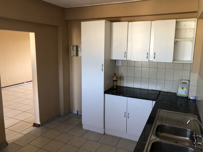 A functional kitchen featuring white built-in cabinetry, dark laminate countertops, a double stainless steel sink, and tiled flooring, ready for modernization.