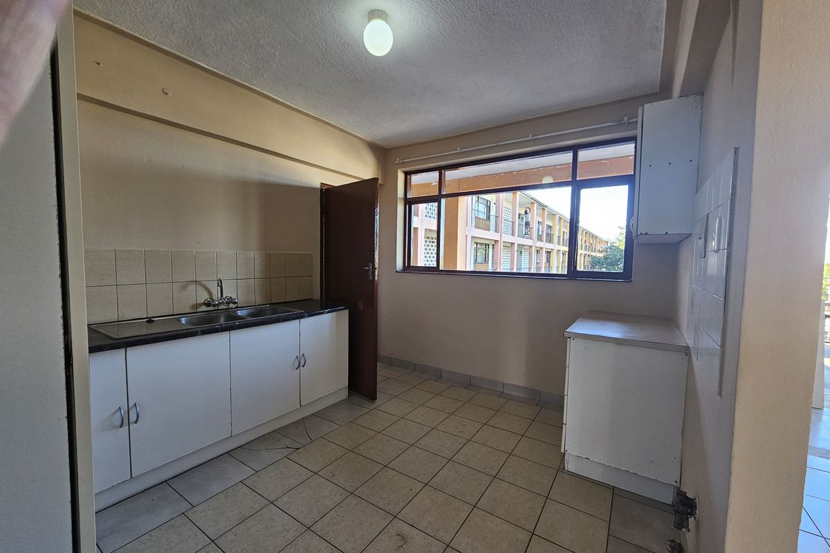 A functional, empty kitchen featuring tiled flooring, built-in base cabinetry with laminate countertops, and a double bowl sink with a tiled splashback.