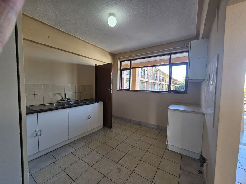 A functional, empty kitchen featuring tiled flooring, built-in base cabinetry with laminate countertops, and a double bowl sink with a tiled splashback.