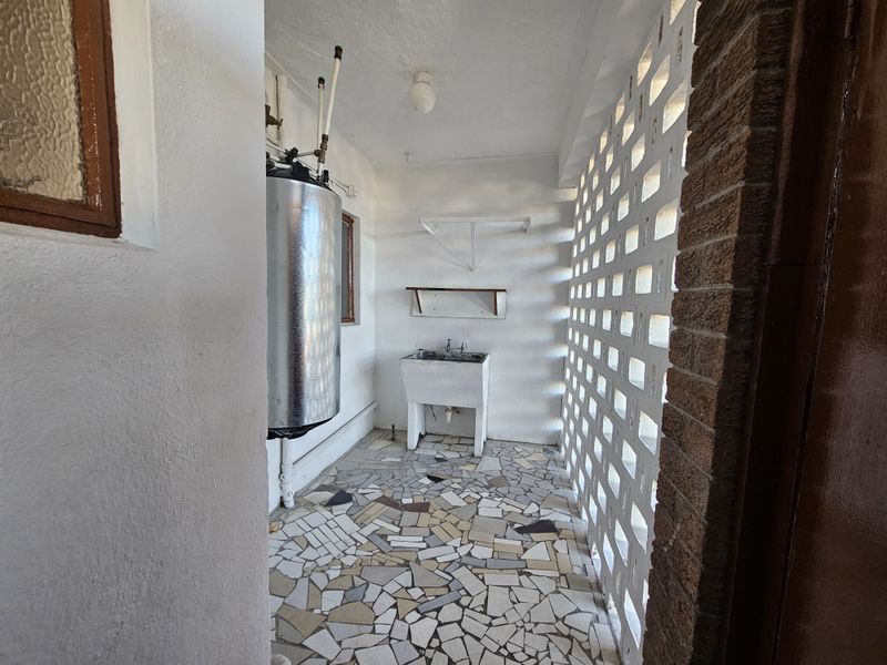A functional laundry area featuring a utility sink, electric water heater, and unique breeze block walling with durable crazy paving flooring.
