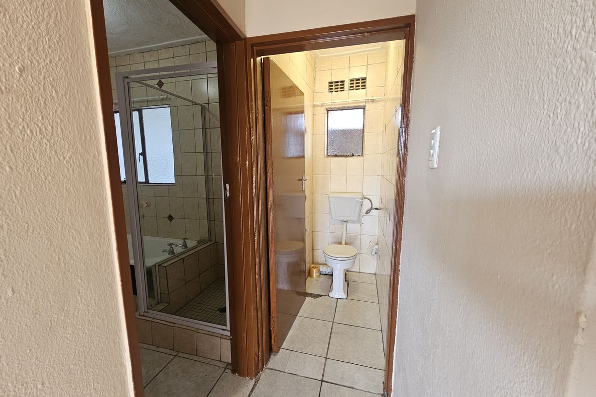 A functional bathroom and separate toilet area featuring tiled finishes, a shower-over-bath configuration, and standard sanitary ware.