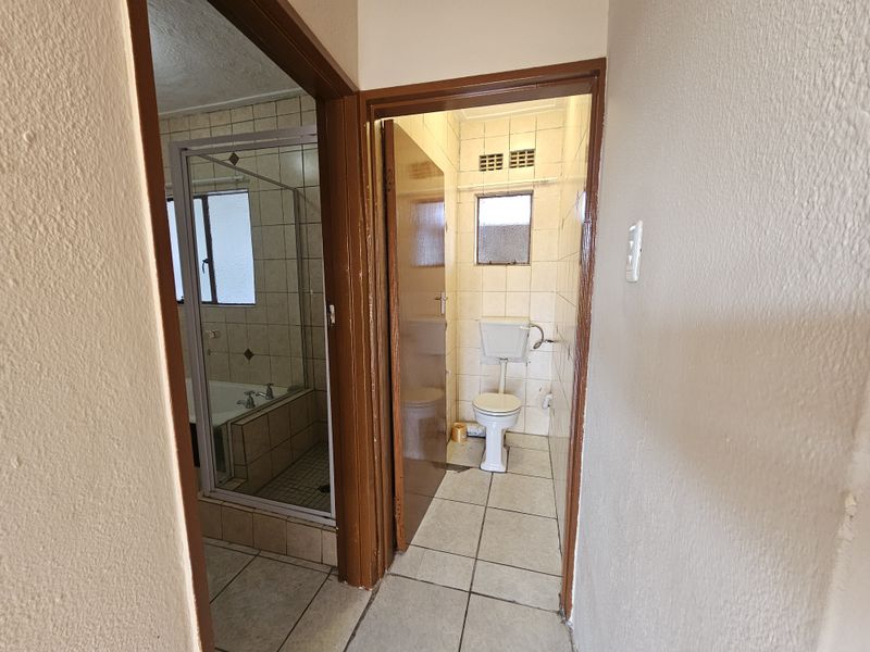 A functional bathroom and separate toilet area featuring tiled finishes, a shower-over-bath configuration, and standard sanitary ware.