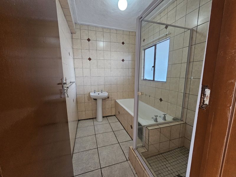 A dated bathroom featuring a pedestal basin, built-in bathtub, and a separate glass-enclosed shower area with ceramic tiling throughout.