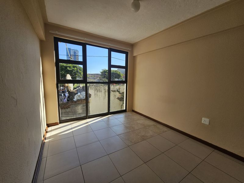 An empty living room featuring large aluminium-framed windows, ceramic tiled flooring, and neutral wall finishes, offering a blank canvas for interior design.