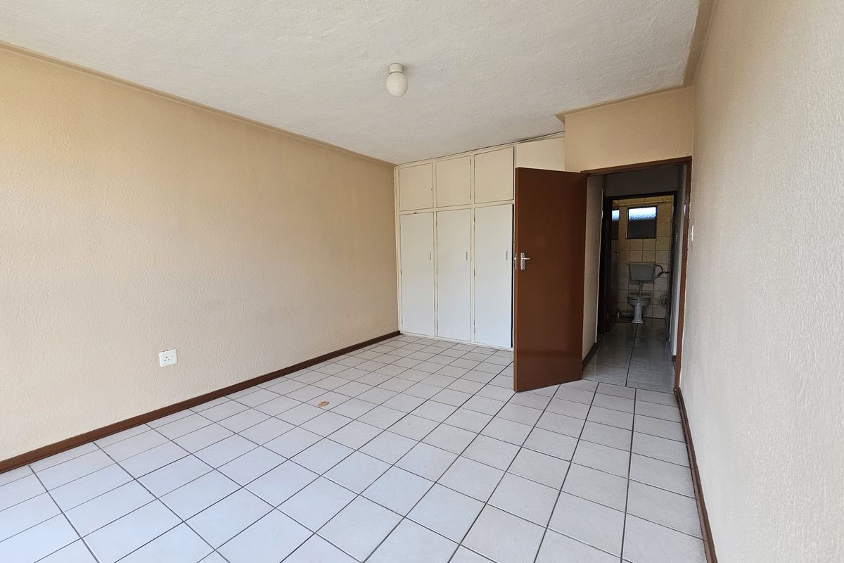 An empty bedroom featuring tiled flooring, built-in cupboards, and direct access to an en-suite bathroom.
