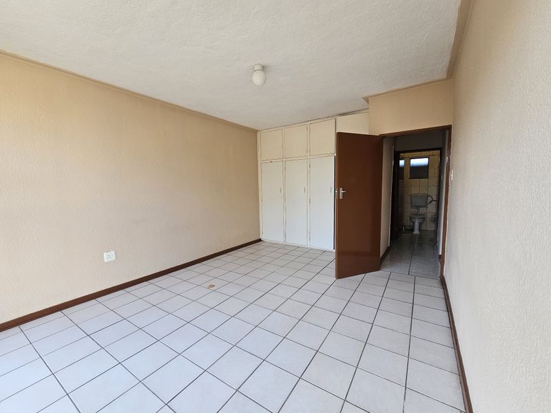 An empty bedroom featuring tiled flooring, built-in cupboards, and direct access to an en-suite bathroom.