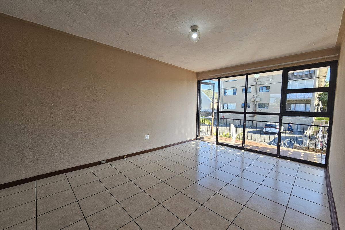 An empty, sunlit living area featuring neutral tiled flooring and large glass sliding doors that provide access to an outdoor balcony space.