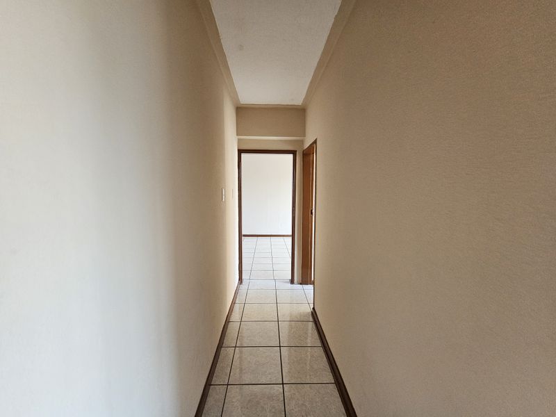 A clean, empty hallway featuring neutral wall finishes and tiled flooring, providing access to adjacent rooms within the apartment.