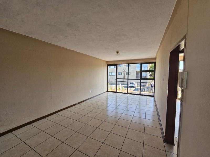 An empty, open-plan living area featuring tiled flooring, large glass sliding doors providing natural light, and an integrated intercom system.