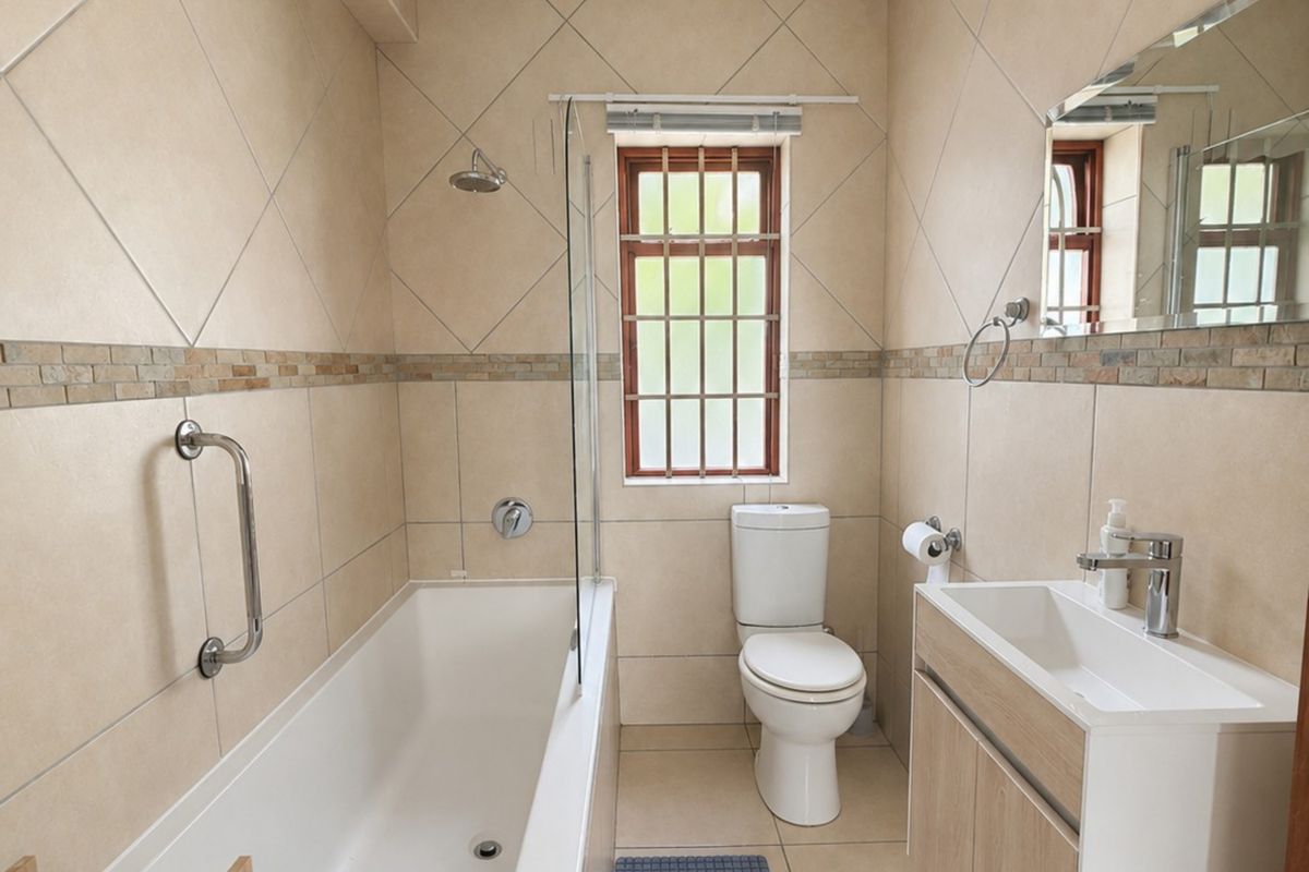 A well-maintained bathroom featuring a bathtub with a glass screen, a modern vanity with basin, and neutral wall tiling.