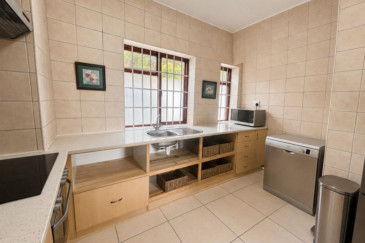 A functional kitchen featuring tiled walls and flooring, built-in cabinetry, a stainless steel sink, and integrated cooking appliances.