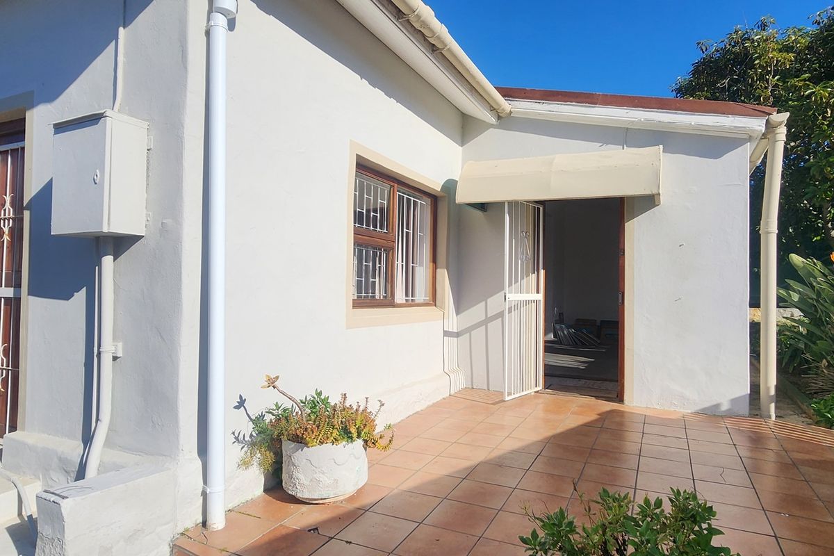 A rear exterior view of the house featuring a tiled patio area, security gates, and window bars, providing access to the interior living space.