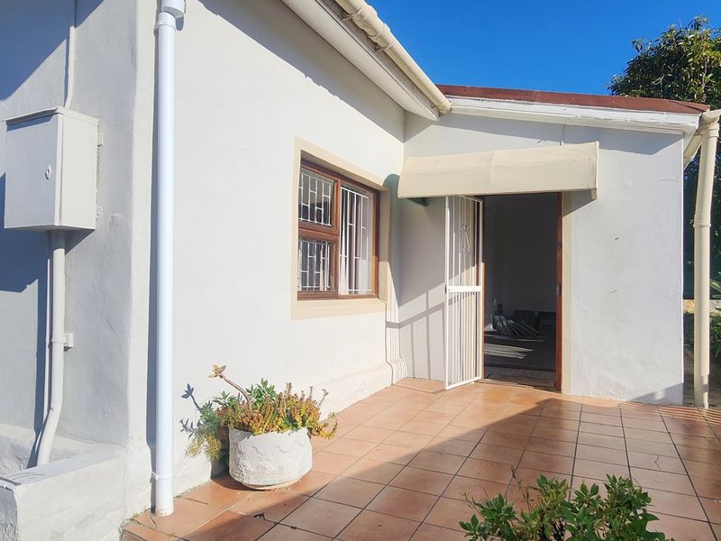 A rear exterior view of the house featuring a tiled patio area, security gates, and window bars, providing access to the interior living space.