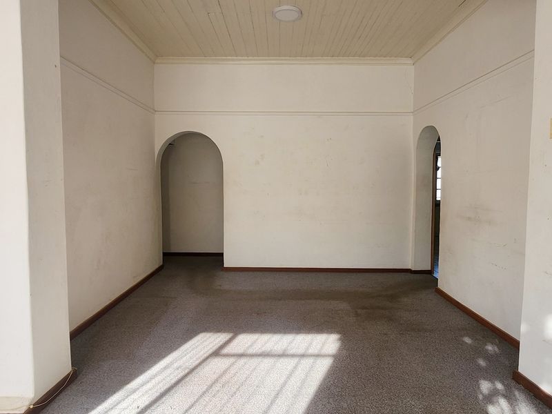 An empty living room featuring classic archways, tongue and groove ceiling detail, and carpet flooring, ready for renovation or staging.