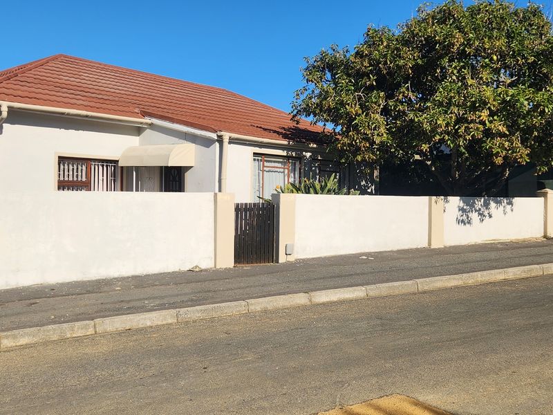 Front elevation of a single-story house featuring a tiled roof, boundary wall with gated access, and security bars on windows.