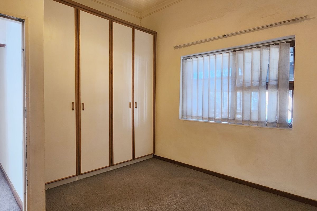 An empty bedroom featuring built-in cupboards, carpeted flooring, and vertical blinds, offering a blank canvas for renovation or restyling.