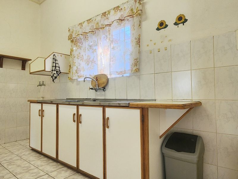 A functional kitchen space featuring built-in cabinetry, a stainless steel sink, and tiled splashbacks, offering a blank canvas for potential renovation and modernization.