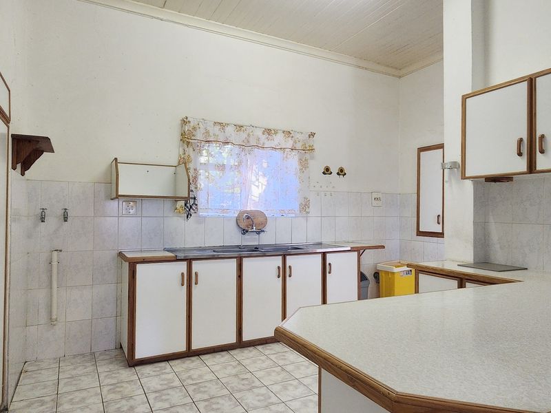 A dated, empty kitchen featuring built-in cabinetry, laminate countertops, tiled backsplash, and tiled flooring, offering significant potential for a modern renovation.