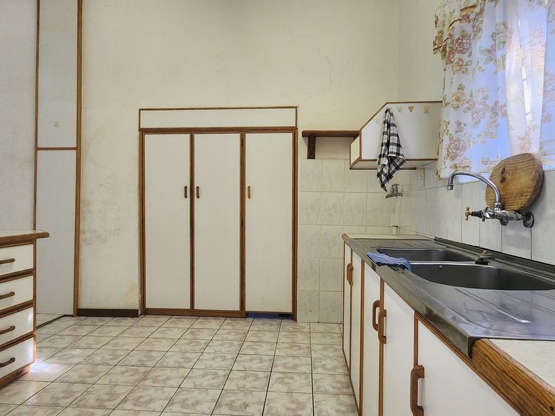 A dated kitchen featuring built-in cabinetry, a double bowl stainless steel sink, and tiled flooring, offering significant potential for modernization and renovation.