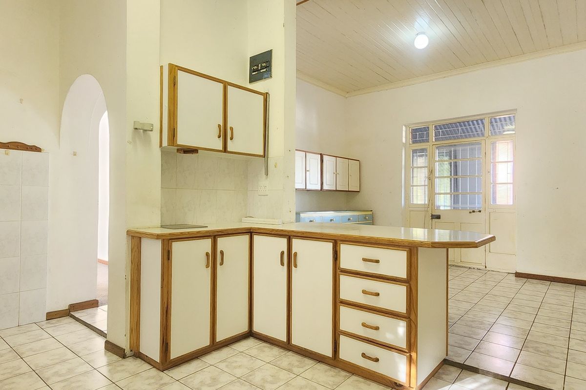 An empty, dated kitchen featuring built-in cabinetry, tiled flooring, and a timber ceiling, offering significant potential for a modern renovation.