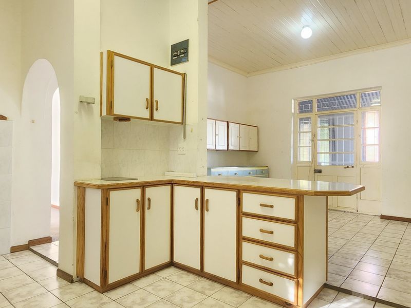 An empty, dated kitchen featuring built-in cabinetry, tiled flooring, and a timber ceiling, offering significant potential for a modern renovation.